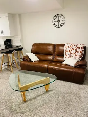 a living room with a brown leather couch and a glass table at Modern Comfort in NW Calgary in Calgary