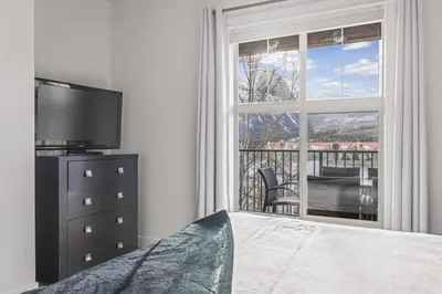a bedroom with a bed and a tv and a window at Serene 2BR Hideaway Hot Tub and Breathtaking Views in Canmore