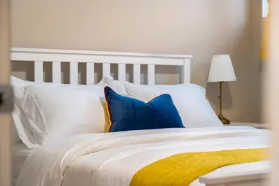 a white bed with blue pillows and a yellow blanket at Panorama Hills Cozy Guest Suite in Calgary