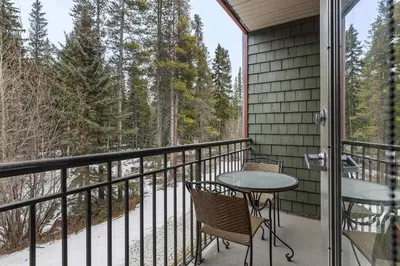 a balcony with a table and chairs and trees at Tranquil Condo In The Trees Spacious 2Bd Hot Tub & Pool in Canmore