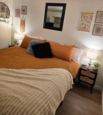 a bedroom with a bed with an orange comforter and a mirror at Small Town Pearl l Charming & Cozy 2 Level Suite Near Red Deer l Yard & BBQ in Penhold