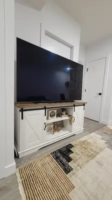 a living room with a large television on a white entertainment center at 2BR 14minsYYC Airport Private Entrance Soft Water System in Calgary