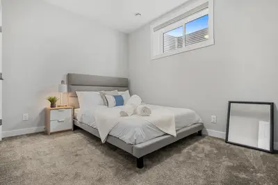 a bedroom with a bed with a mirror and a window at Herron Rise Luxury 1 Bedroom Basement Suite in Calgary