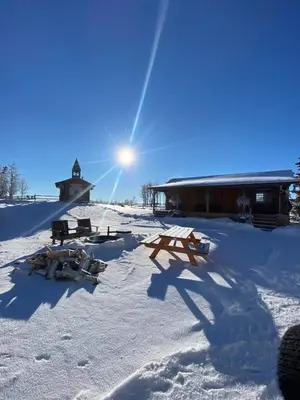 a snow covered area with a building with the sun behind it at The White Tail Cabin - Bear Creek Cabins in Winfield