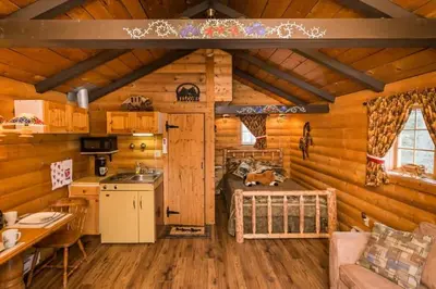 a log cabin kitchen and living room with a bed at The Mustang Cabin - Bear Creek Cabins in Winfield