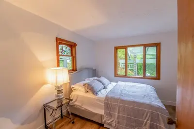 a bedroom with a bed with a lamp and two windows at Picturesque and Comfy Escape with Waterfall View in Garden Bay