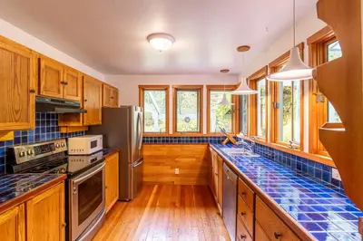 a kitchen with wooden cabinets and blue tiles on the counters at Picturesque and Comfy Escape with Waterfall View in Garden Bay
