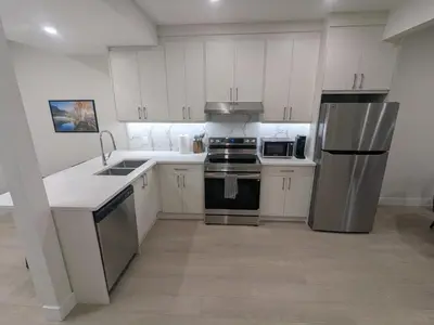 a kitchen with white cabinets and stainless steel appliances at Greystone Retreat - Walk to River & Downtown in Cochrane