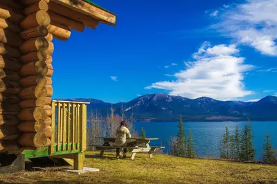 a person sitting on a picnic table in front of a lake at Southern Lakes Resort in Tagish