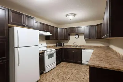 a kitchen with wooden cabinets and a white refrigerator at Super 8 by Wyndham Fort McMurray in Fort McMurray