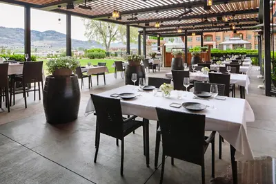 a restaurant with white tables and chairs and mountains in the background at Watermark Beach Resort in Osoyoos