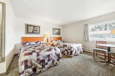 a bedroom with two beds and a table and a window at Guest House Inn & Suites in Edson
