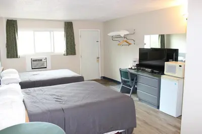 a hotel room with two beds and a desk with a tv at Plains Motor Inn in Stettler