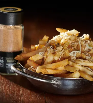 a metal bowl of french fries with seasoning on a table at Acclaim Hotel by CLIQUE in Calgary