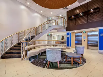 a lobby with a staircase and tables and chairs at Holiday Inn Express & Suites Langley by IHG in Langley