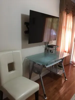 a glass table with a chair and a television on a wall at Garden Bridge House in Sechelt