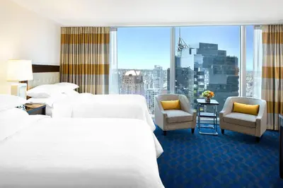 a hotel room with two beds and chairs and a large window at Sheraton Vancouver Wall Centre in Vancouver