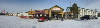 a snow covered street with cars parked in front of a building at Sundre Motor Inn in Sundre