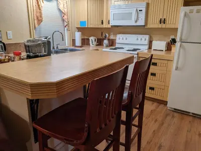 a kitchen with a wooden island with chairs and a refrigerator at Third Mission Heritage Suites in Peace River