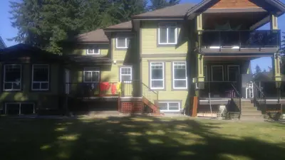 a yellow house with a porch and a yard at Vancouver Jenny's Guesthouse in Coquitlam