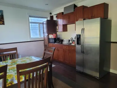 a kitchen with a table and a stainless steel refrigerator at Vancouver Jenny's Guesthouse in Coquitlam