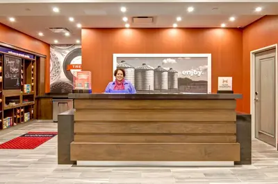 a woman standing behind a counter in a store lobby at Hampton Inn & Suites by Hilton Grande Prairie in Grande Prairie