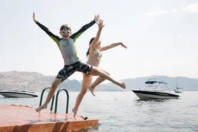 two people jumping off a dock into the water at Peachland Beach Resort in Peachland