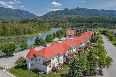 an aerial view of a resort with a river and mountains at Riverside by StayIn in Fernie