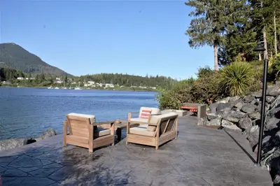 two chairs and a table next to a body of water at Private Oceanfront Cabin With Hot Tub Doc Holiday Cabin in Ucluelet