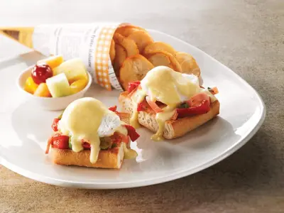 a white plate with two breakfast sandwiches and a basket of bread at Holiday Inn Hotel & Suites Calgary South - Conference Ctr by IHG in Calgary