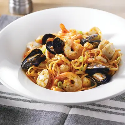 a white plate of pasta with shrimp and mussels at Holiday Inn Hotel & Suites Calgary South - Conference Ctr by IHG in Calgary