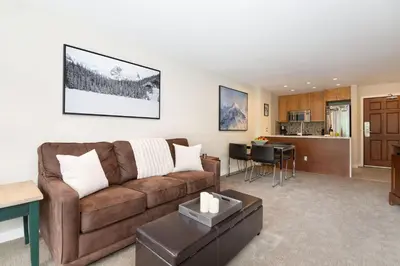 a living room with a brown couch and a kitchen at Aspens Mountain Side Resort in Whistler