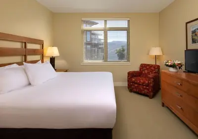 a bedroom with a bed and a chair and a television at The Cove Lakeside Resort in West Kelowna
