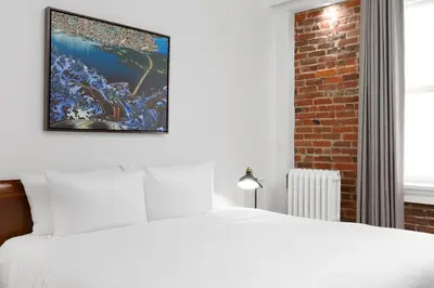 a bedroom with a white bed and a painting on the wall at Victorian Hotel in Vancouver