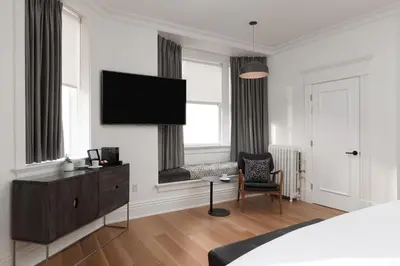 a bedroom with a tv on the wall and a chair at Victorian Hotel in Vancouver