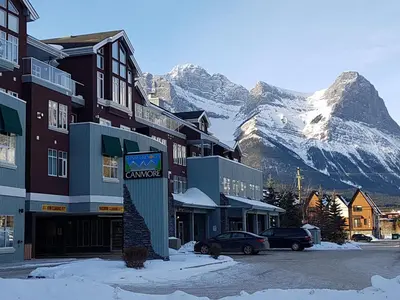 a snow covered mountain in front of a town with buildings at Sunset Resorts Canmore and Spa in Canmore
