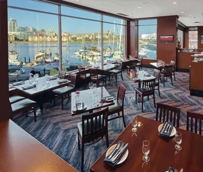 a restaurant with tables and chairs and a view of a harbor at Coast Victoria Hotel & Marina by APA in Victoria