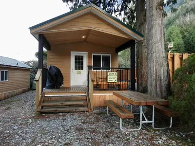 a wooden cabin with a bench and a tree at Camperland RV Resort & Cabins in Rosedale