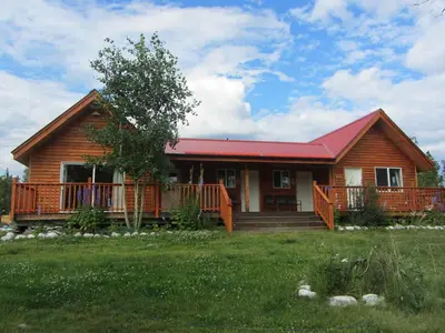 a log home with a porch and a red roof at Eagle Bear Lodge in Tatla Lake