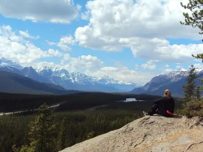 a woman sitting on top of a rock looking at the mountains at Sunwapta Falls Rocky Mountain Lodge in Jasper