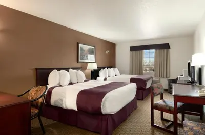 a hotel room with two beds and a desk at Ramada by Wyndham Red Deer Hotel & Suites in Red Deer