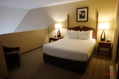 a hotel room with a bed and a chair and lamps at Ramada by Wyndham Kelowna Hotel & Conference Center in Kelowna