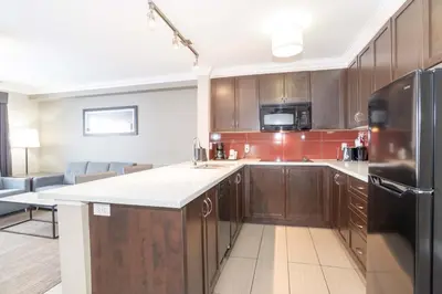 a kitchen with wooden cabinets and a black refrigerator at Sandman Hotel and Suites Abbotsford in Abbotsford