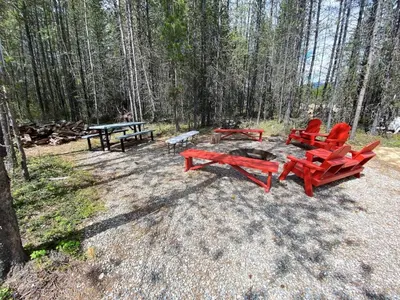 a group of red chairs and a picnic table in the woods at Aspen in Valemount