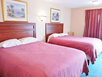 two beds in a hotel room with red sheets at Alpine Motel in Kamloops