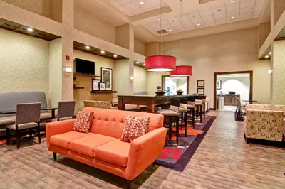 a waiting room with an orange couch and tables and chairs at Hampton Inn & Suites Red Deer in Red Deer