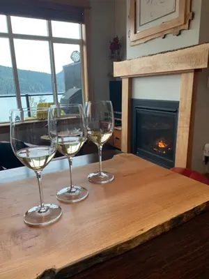 three wine glasses sitting on a wooden table with a fireplace at Bjørn Holm in Port Renfrew
