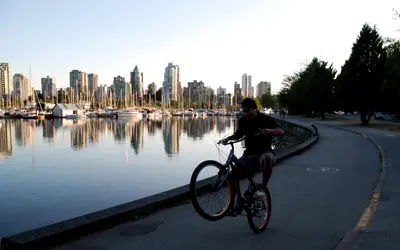 a man riding a bike next to a body of water at Rosellen Suites at Stanley Park in Vancouver