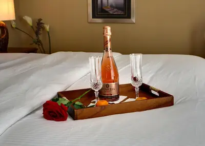 a bottle of champagne and two wine glasses on a bed at Rosellen Suites at Stanley Park in Vancouver