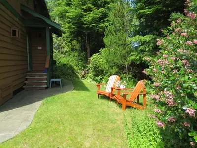 two wooden chairs and a table in the grass at Summerhill Guest House in Tofino